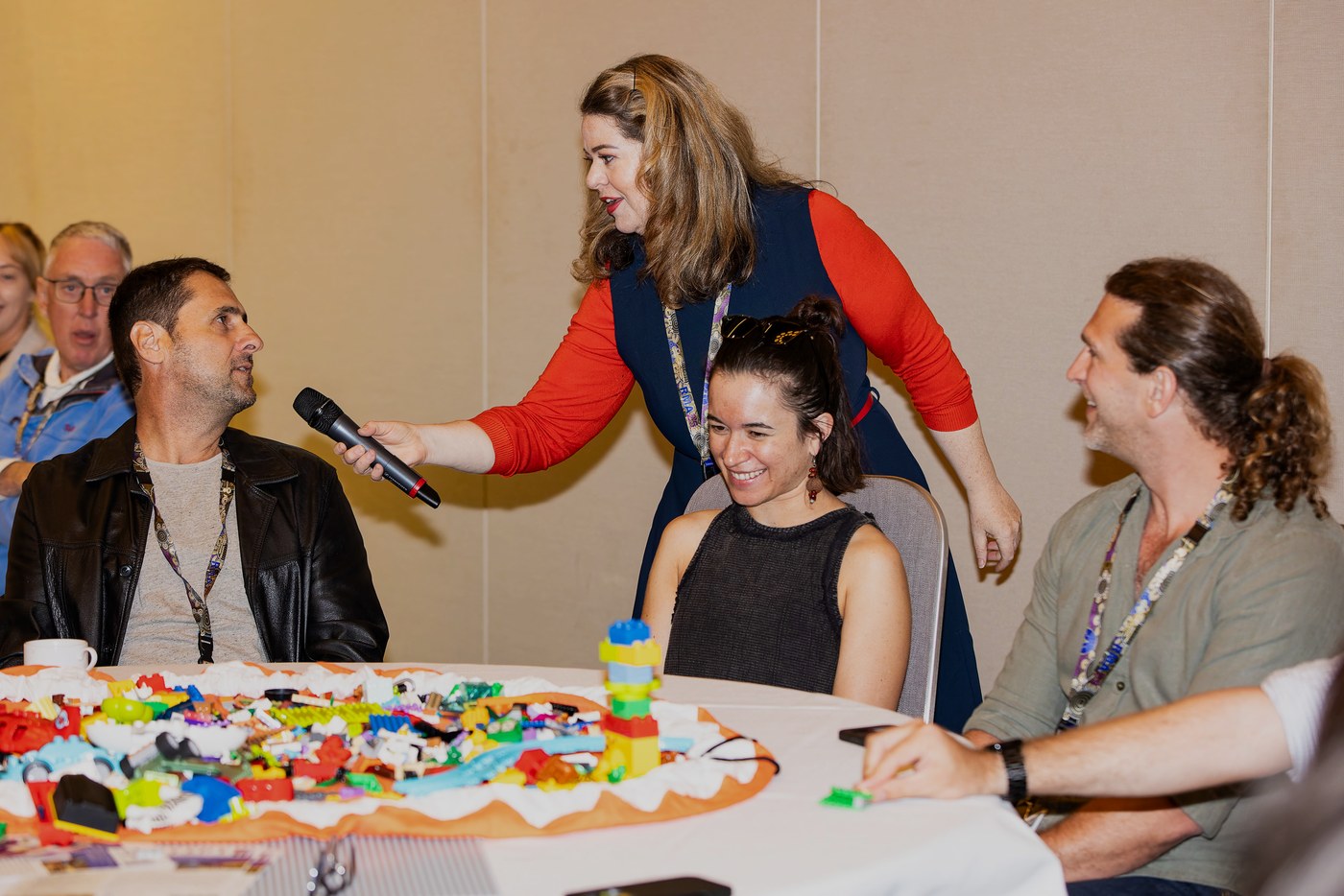 Tanya holding a microphone for a conference delegate as the group talks together around a table of LEGO® bricks