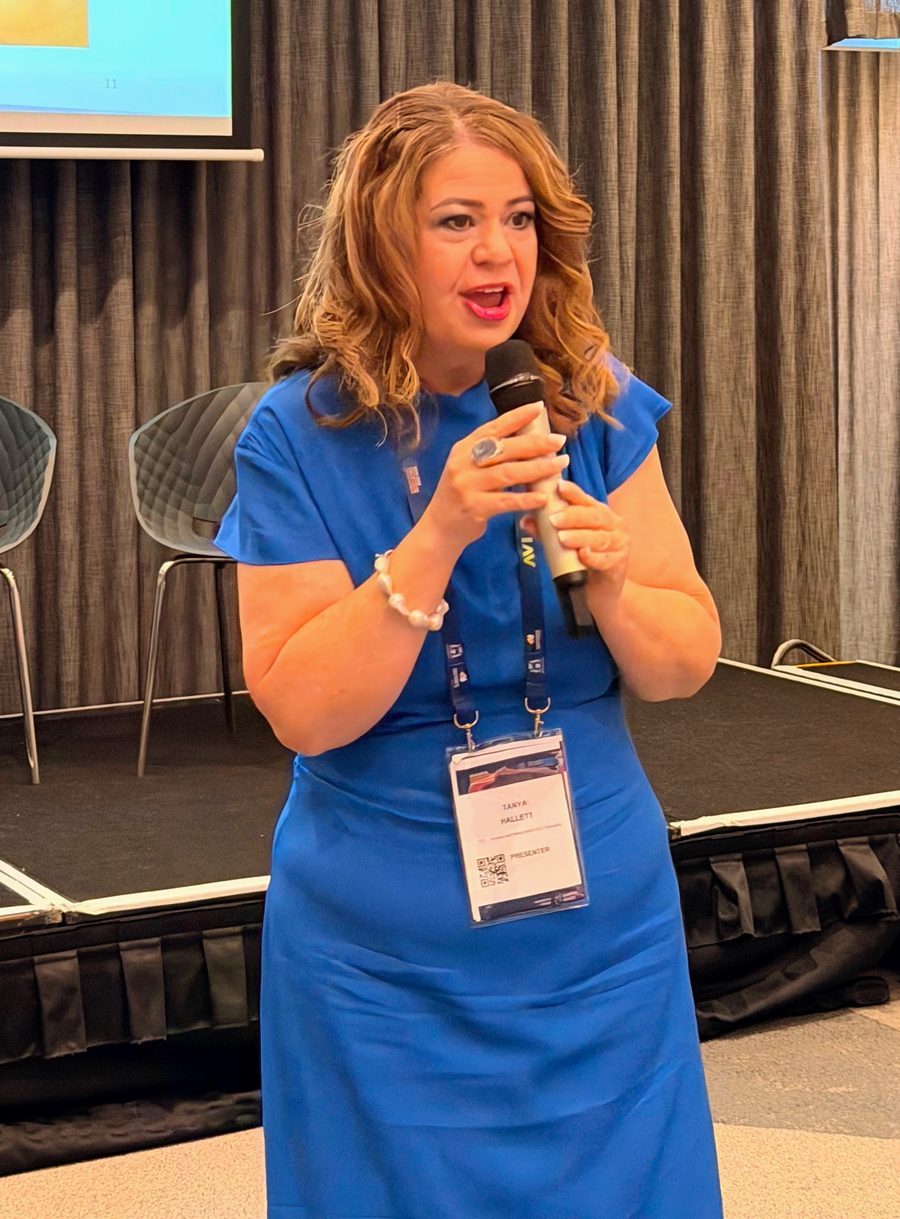 Tanya Hallett speaking into a microphone on stage at a conference